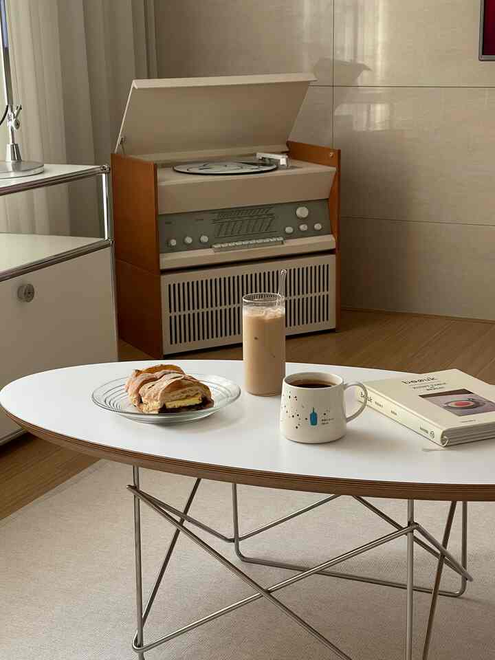 ホワイトとブラウンの色調のリビング、ヴィンテージのレコードプレーヤーと飲み物とペストリーが置かれたコーヒーテーブルが配置された雰囲気のあるおうちカフェ空間