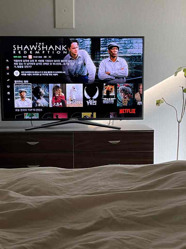 ホワイトとブラウンのトーンが特徴の寝室、ベッドの掛け布団カバーとテレビ台が配置された落ち着いたリラックス空間