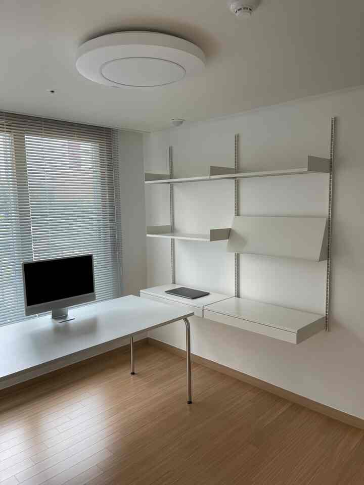 白を基調とした明るいホームオフィス、広い白いデスクとシステム棚が配置されたミニマルで清潔感のあるインテリア