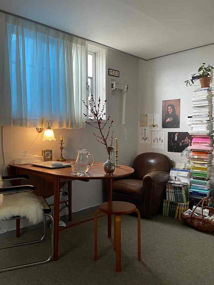 白と茶色の色調の書斎型の部屋、木製デスクとレザーのアームチェア、積み重ねられた本と観葉植物が配置された雰囲気のあるインテリア