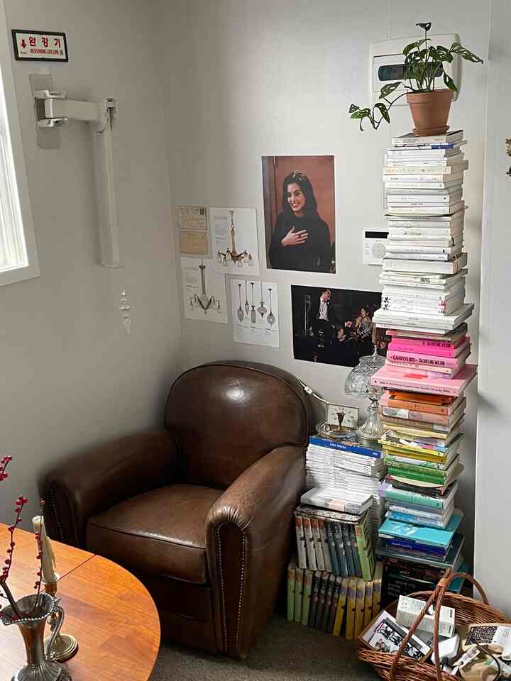 ブラウンレザーのソファと積み上げられた本、壁付け照明のある落ち着いたリビングのコーナー