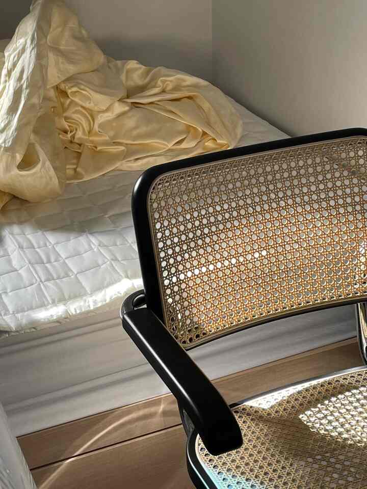 柔らかなアイボリーの寝具とミニマルな黒いラタンチェアがある落ち着いた寝室空間