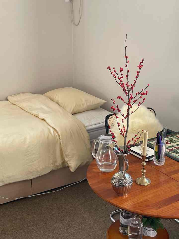 アイボリー色調の寝室、木目調の丸テーブルとベッドが調和したシンプルで自然な雰囲気のインテリア