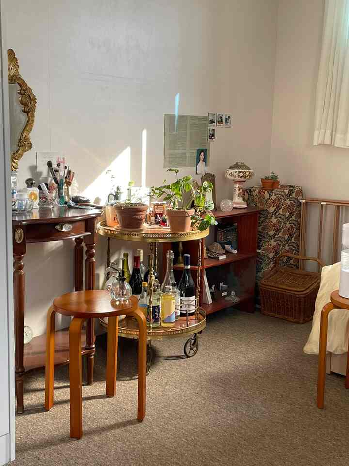 暖かいブラウンの木目調とナチュラルスタイルの寝室コーナー、円形のトロリーと化粧台、キャビネットが配置された印象的な空間