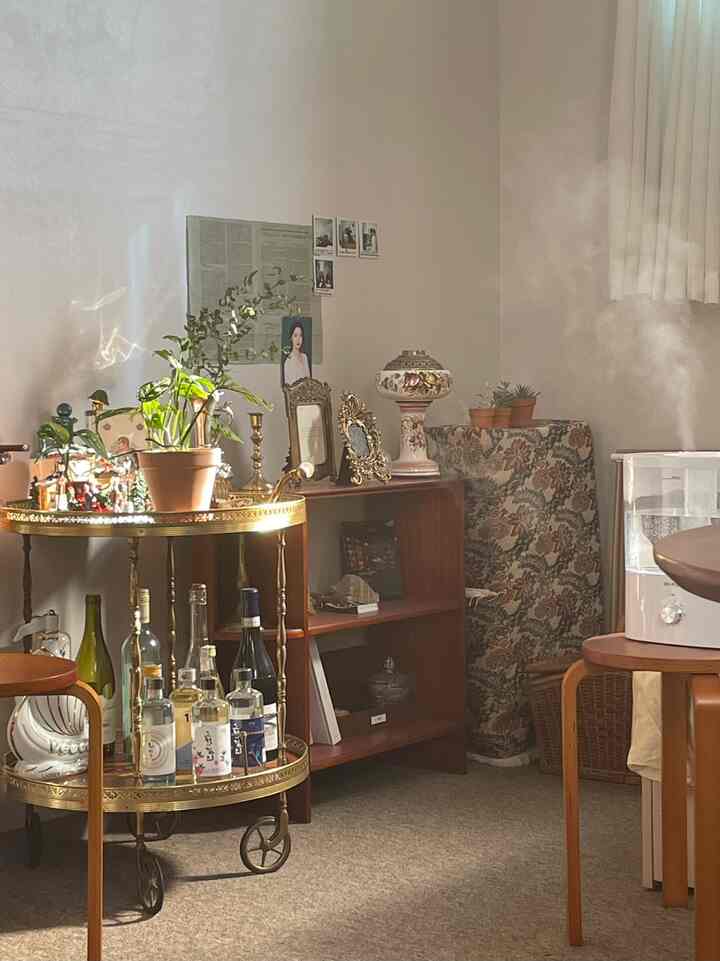 ナチュラルカラーの小さな部屋、ビンテージスタイルのホームバーやサイドボード、植物と照明が配置された雰囲気のあるインテリア