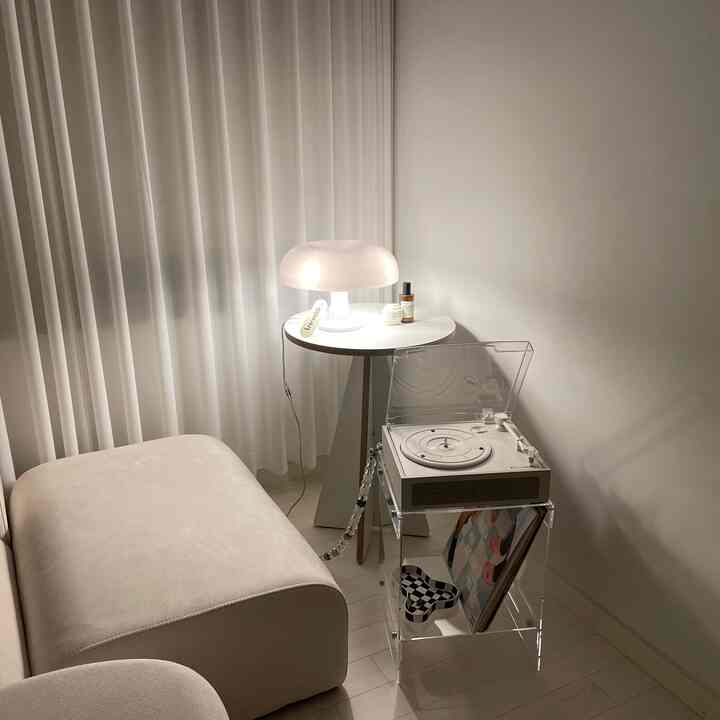 白とベージュのトーンのリビング、透明なアクリルサイドテーブルの上に小さくシンプルなターンテーブルとアルテミデの照明が配置された雰囲気のあるインテリア