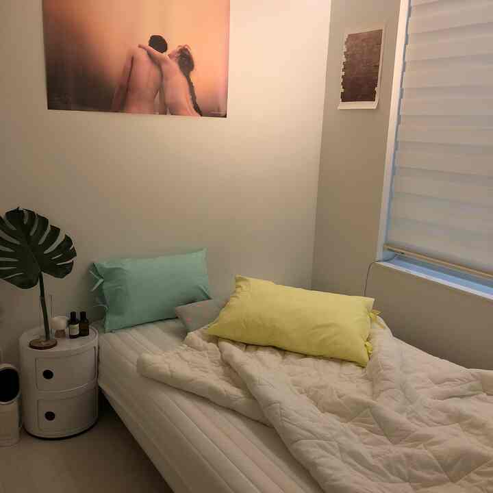 白とパステル調の自然な色合いの6畳の寝室、円形の収納ナイトテーブルとカラフルな枕が配置された1人暮らしの温かみのある空間