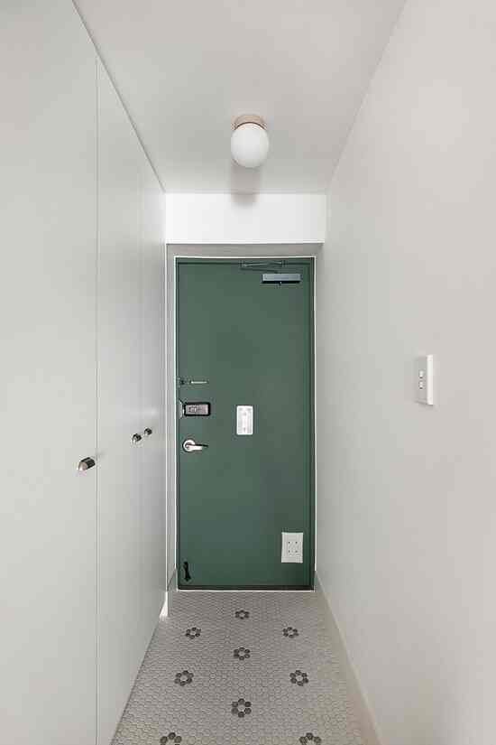 白い壁と靴箱が配置された緑色の玄関ドアがある縦長の廊下空間