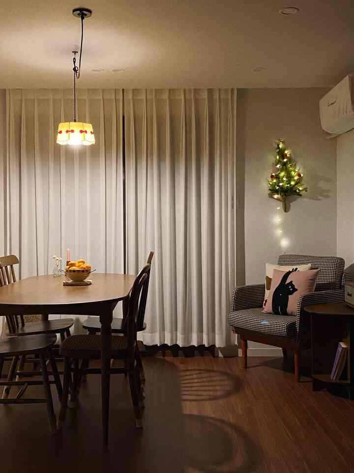 暖かい木目調と白いカーテンが調和したダイニングルーム、居心地の良いペンダントライトと壁のクリスマスツリーが雰囲気を演出