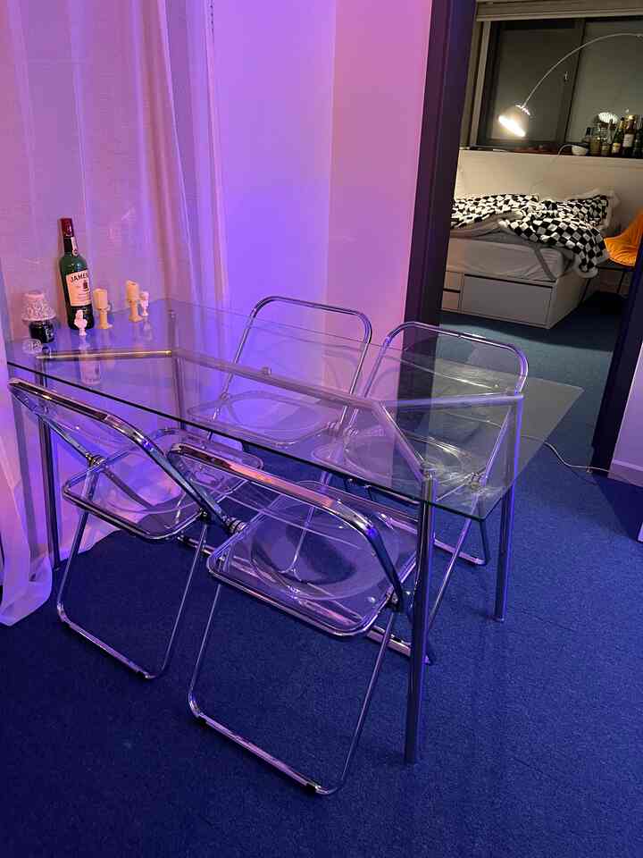 ブルーのカーペットと透明なガラス製ダイニングテーブルとチェアが配置された狭いワンルーム、モダンで清潔感のあるインテリア