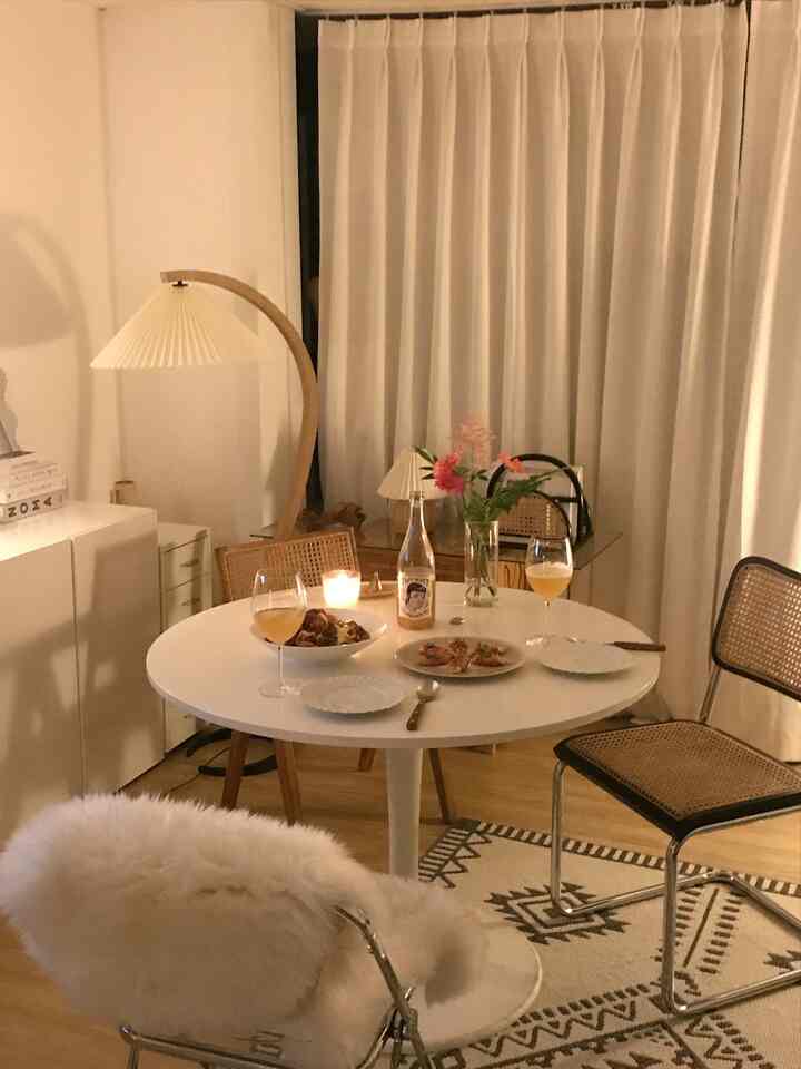 白と木目調のダイニングルーム、円形テーブルとラタンのアームチェアが配置された雰囲気のあるホームパーティー空間