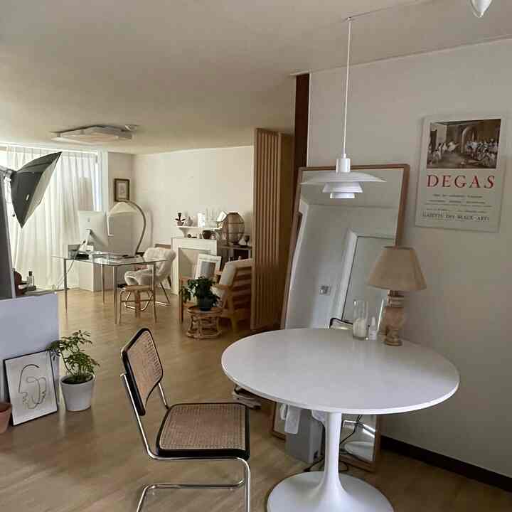 ナチュラルなウッドフロアとホワイトの円形テーブルがあるリビング、ルイスポールセンのペンダントライトと大型の全身鏡が配置されたシンプルなインテリア