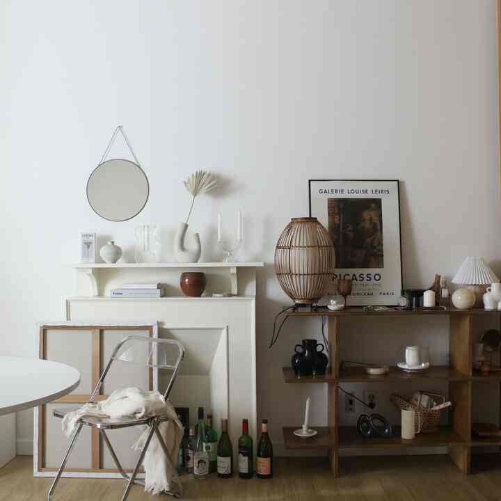 ホワイトトーンの壁とナチュラルウッドの棚が調和するリビング、透明な椅子と多様なオブジェが配置されたシンプルでヴィンテージ感のあるインテリア