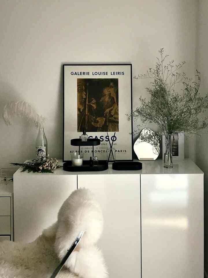 白を基調としたリビング空間、シンプルなキャビネットの上に額縁や花瓶、自然な植物が配置されたミニマルなインテリア