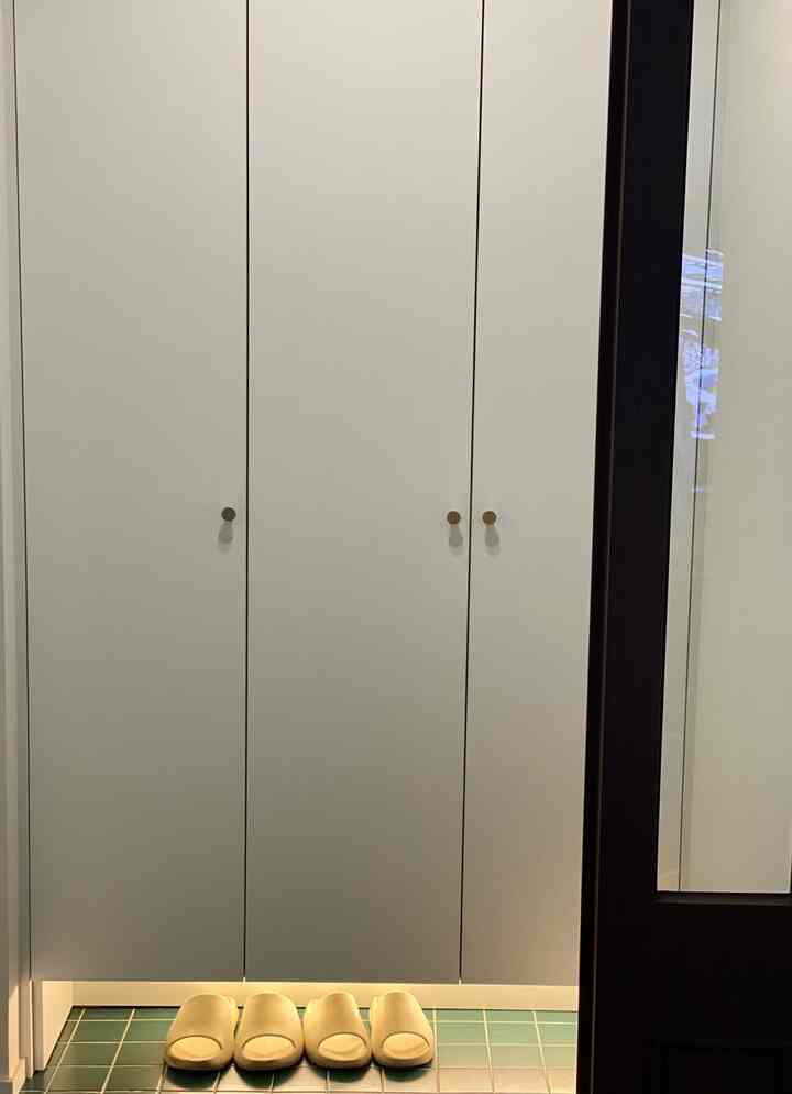 ホワイトのマット仕上げシューズラックが配置された玄関、ゴールドの取っ手とグリーンタイル床が調和するモダンな空間