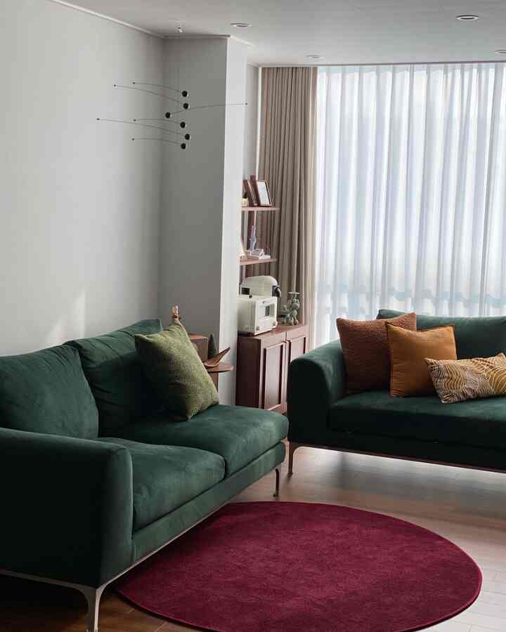 深緑のソファと円形のバーガンディラグが配置された、明るく広々としたリビングルーム