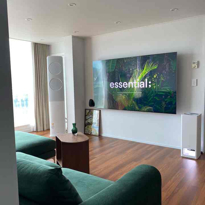 ダークグリーンのソファと木目調の床があるシンプルなリビング、大型のサムスン85インチテレビが壁に掛けられています。