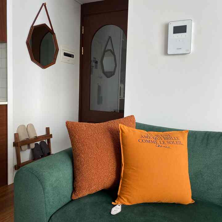 深緑のソファとオレンジのクッションが配置された玄関とリビングが繋がるナチュラルモダンなインテリア