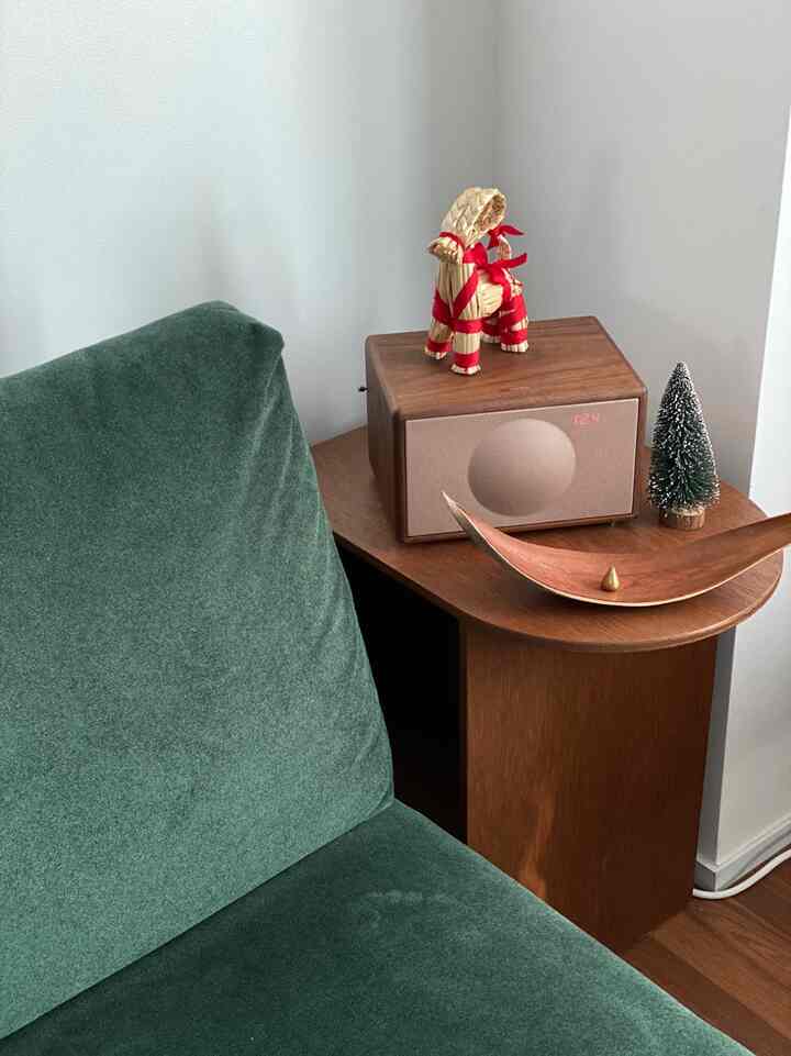 ダークグリーンのソファとウォールナットの木目調サイドテーブルにブルートゥーススピーカーとクリスマスオーナメントが置かれたナチュラルなコーナーインテリア