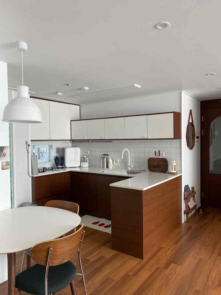 ホワイトとウォールナットの木目調のキッチン、丸いダイニングテーブルと椅子が配置されたシンプルで落ち着いた雰囲気のインテリア