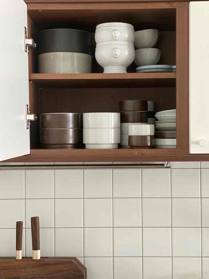 ナチュラルな木目調の壁吊り戸棚に様々な色の器が整然と並べられた、清潔感のあるキッチン空間