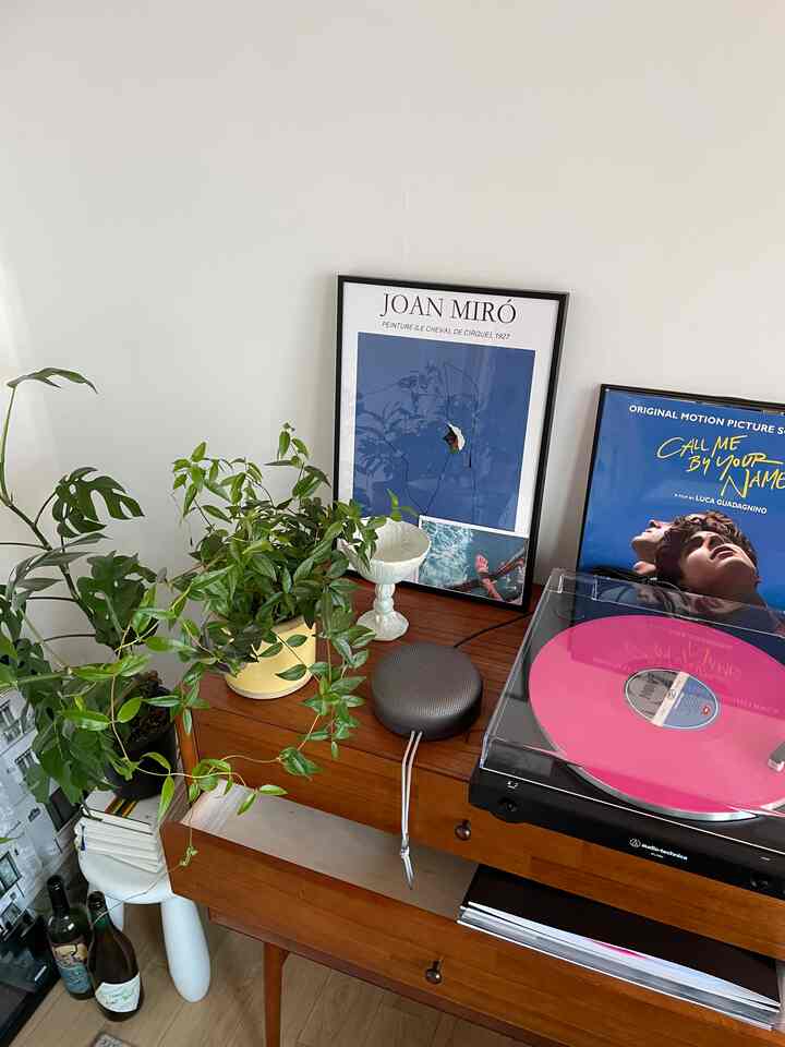 ブラウンのチェストの上にブルーとホワイトの額が置かれ、植物とターンテーブルが配置された雰囲気のあるインテリア