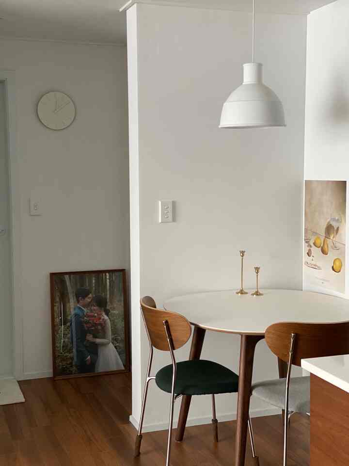 白と木目調が調和するダイニング、丸テーブルに深緑とグレーのファブリックチェアが配置された印象的で自然な空間