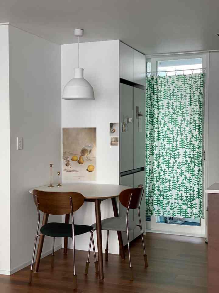 ホワイトとグリーンの色調のモダンダイニング、丸いダイニングテーブルと2つの椅子、パターンのカーテンが配置された雰囲気のあるインテリア