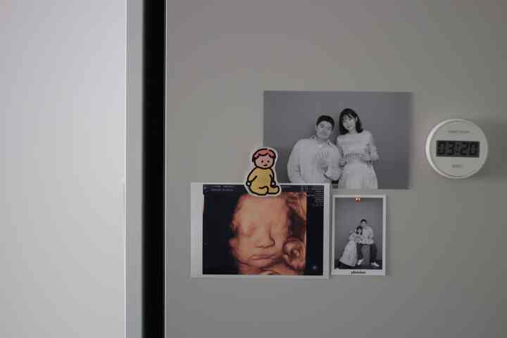 グレーの冷蔵庫の扉に家族写真と妊娠中の超音波写真、シンプルな無印良品のキッチンタイマーが配置された印象的な空間