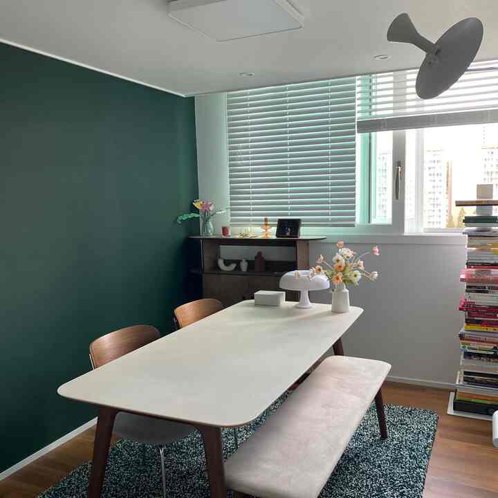 グリーンのアクセントウォールとホワイトトーンのダイニングルーム、木製の椅子とベンチが配置された落ち着いた食事空間