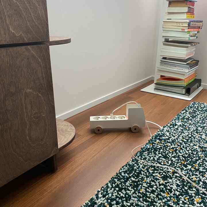 温かみのある木目調の床と緑色のアクセントラグが敷かれたダイニング、トラック型のマルチタップが置かれた居心地の良い空間