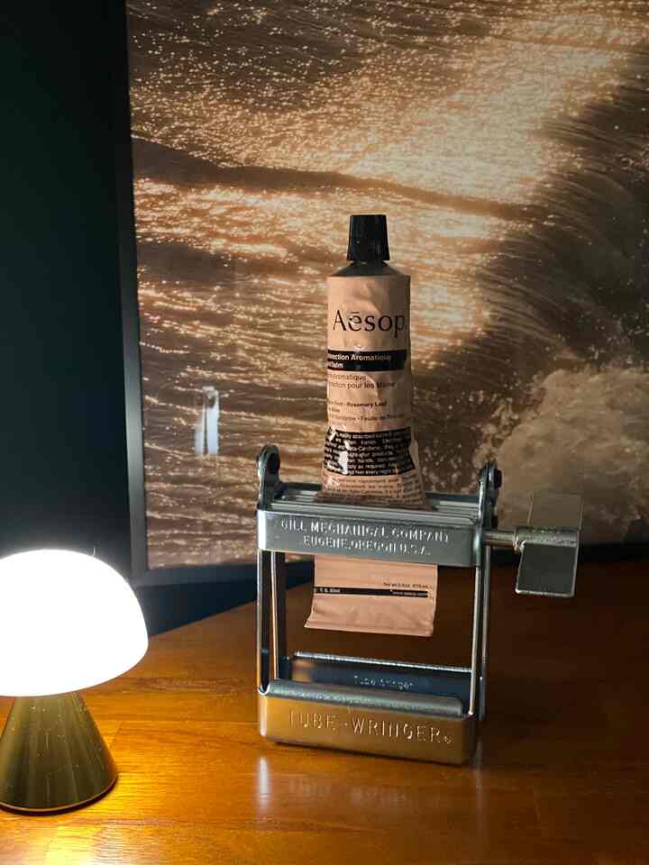 温かみのあるブラウン調の寝室テーブルにチューブ絞り器とイソップのハンドクリームが配置された雰囲気のあるインテリア