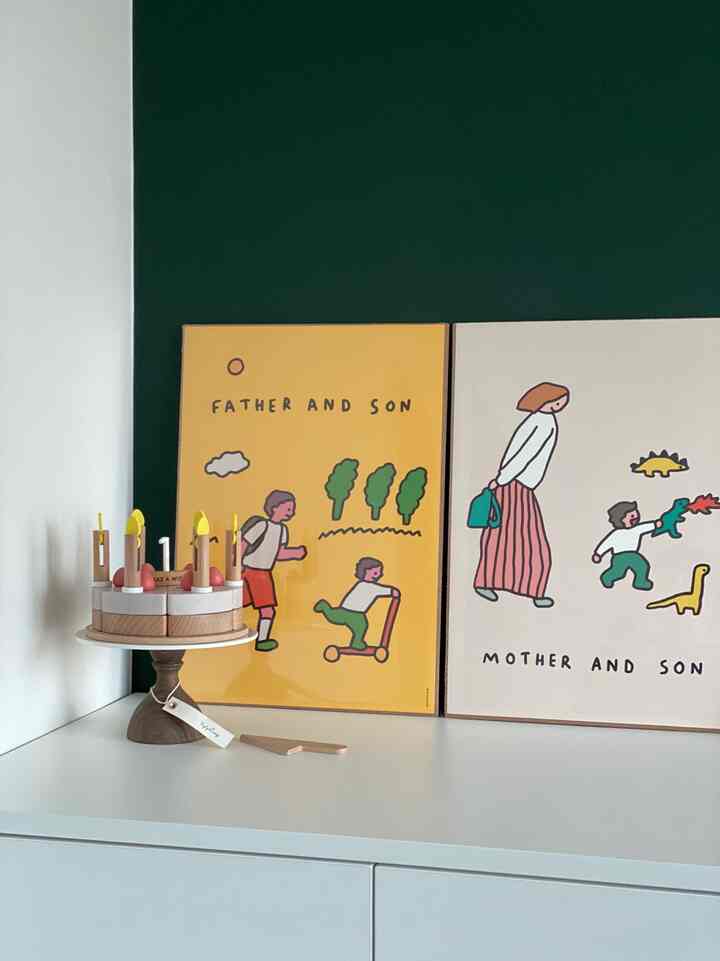 すっきりとした白いクローゼットの上に黄色とベージュのポスターと木製のケーキのおもちゃが置かれた赤ちゃんの部屋の雰囲気のある空間