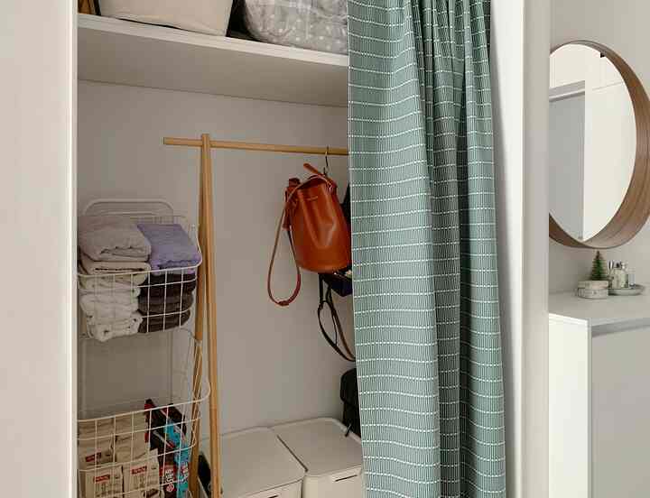 ホワイトと木目調の調和があるベランダの玄関、ウッドハンガーラックと丸い壁掛け鏡、整った収納バスケットが清潔な収納空間を演出