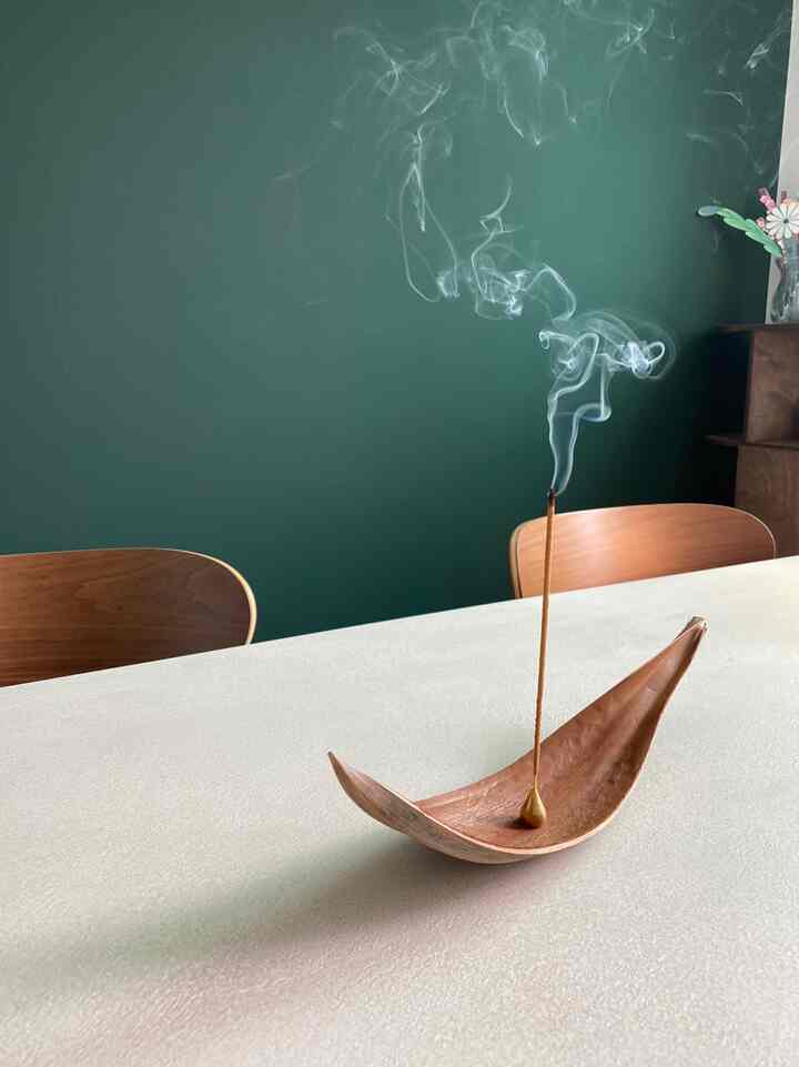 深緑の壁とブラウンの木製椅子があるダイニングルーム、テーブルにはお香とホルダーが置かれている