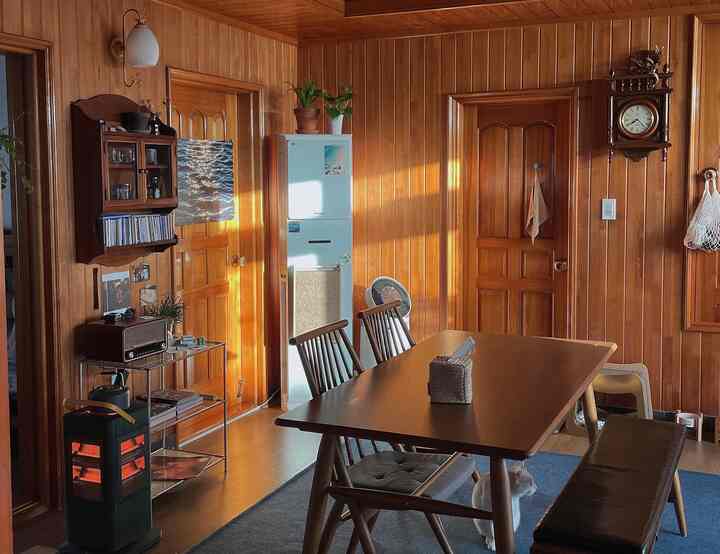 温かみのあるブラウンの木目調ダイニングルーム、中央にダイニングテーブルと椅子が配置され、床に猫が座っている雰囲気のある空間