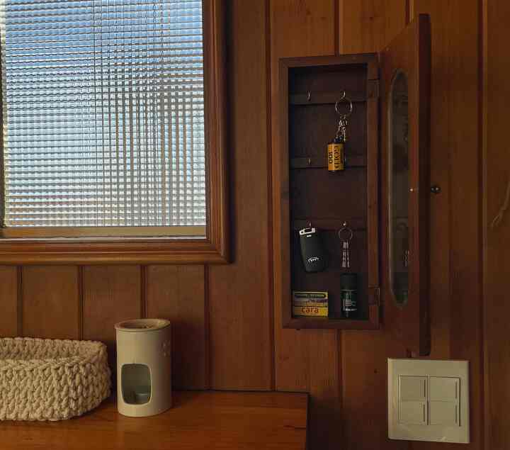 ウッドトーンの壁とデスクにヴィンテージの鍵収納と白いアロマポットが配置された落ち着いた空間