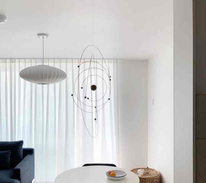 白を基調としたダイニング、ネイビーのソファと個性的なモビールペンダントライトが配置されたシンプルな空間