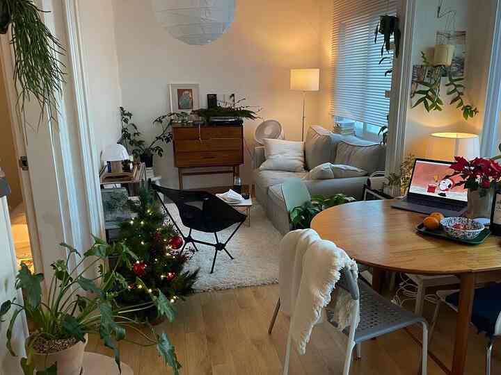 ホワイトとウッドトーンが調和した一人暮らしのリビング・ダイニング、ソファと円形ダイニングテーブル、小さなクリスマスツリーが温かな雰囲気を演出