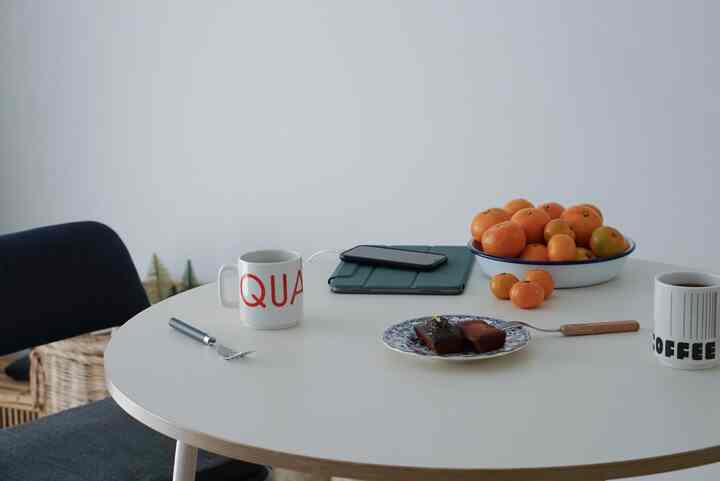 白を基調としたダイニング、丸いテーブルにコーヒーカップと果物のボウルが置かれたシンプルなインテリア