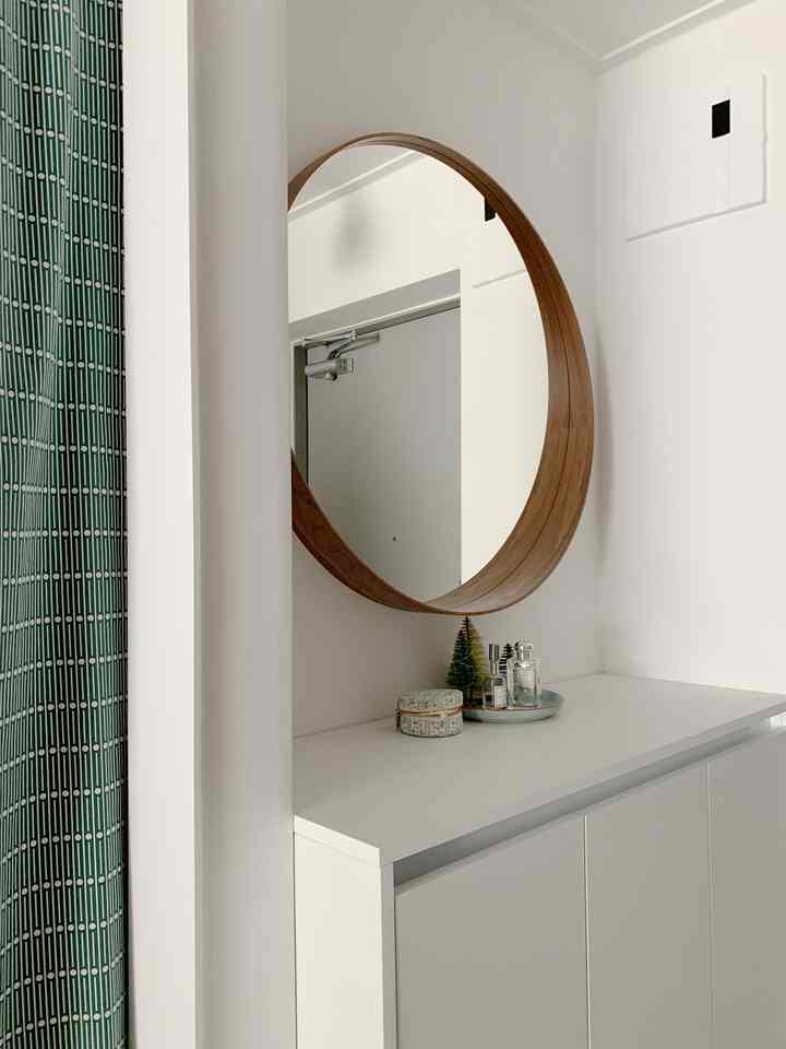 ホワイトと木目調が調和したシンプルな玄関、丸い鏡と収納キャビネットが配置され、清潔感のある雰囲気のインテリア。