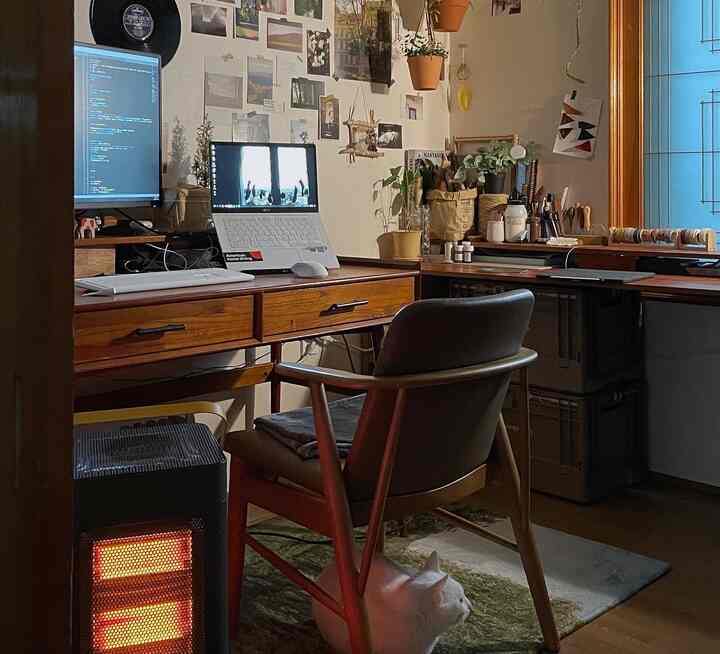 温かみのあるウッド調とベージュ色のコンパクトなホームオフィス、机と椅子、電気暖房器具、猫がいる居心地の良い作業空間