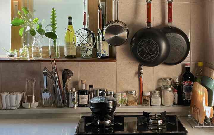 温かみのあるベージュと木目調のキッチン、ガスコンロとヴィンテージ調理器具、植物とガラス瓶が配置された雰囲気のある空間