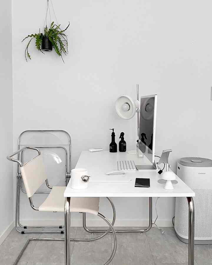 白を基調としたホームオフィス、メタルフレームの椅子と透明な折りたたみ椅子が配置されたモダンな作業空間