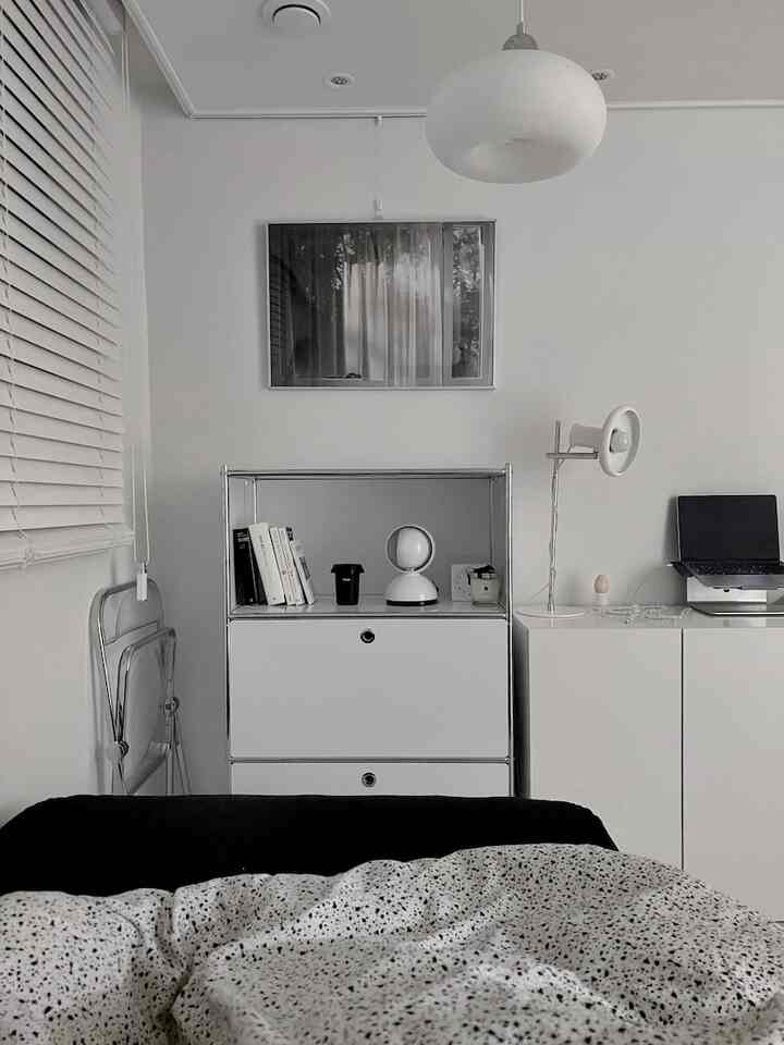 ホワイトとブラックを基調とした寝室、白いキャビネットとデスク上のノートパソコンが配置されたシンプルでモダンなインテリア