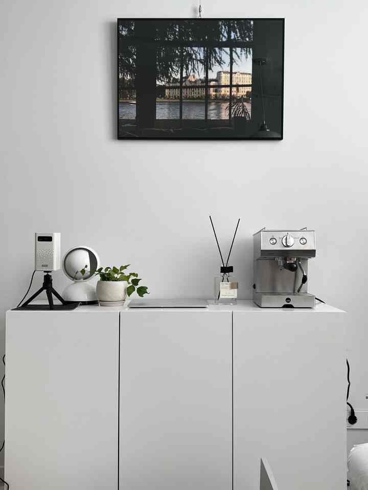 明るいホワイトトーンのモダンなキッチン空間、コーヒーマシンとディフューザーが置かれたすっきりしたカウンターと壁のポスターが配置されたインテリア