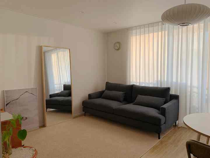 ナチュラルカラーとダークグレーのソファがあるシンプルモダンなリビング、大型鏡と白いカーテンが空間の広がりを演出