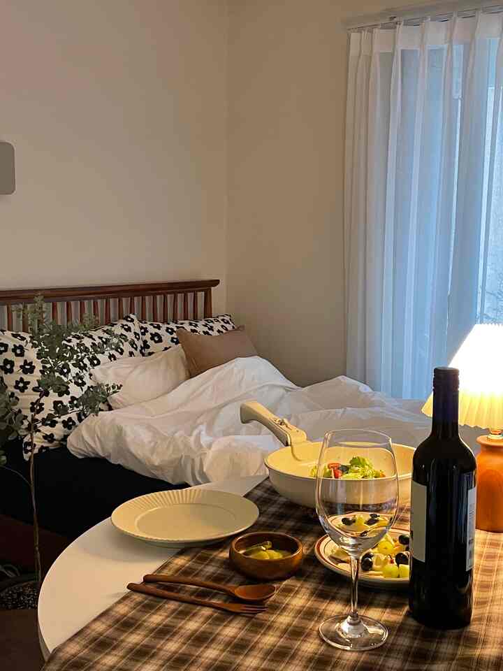 白と茶色のトーンが調和した寝室とダイニングルームの空間、木製ベッドフレームとテーブルのワインと食器が温かみのある雰囲気を演出