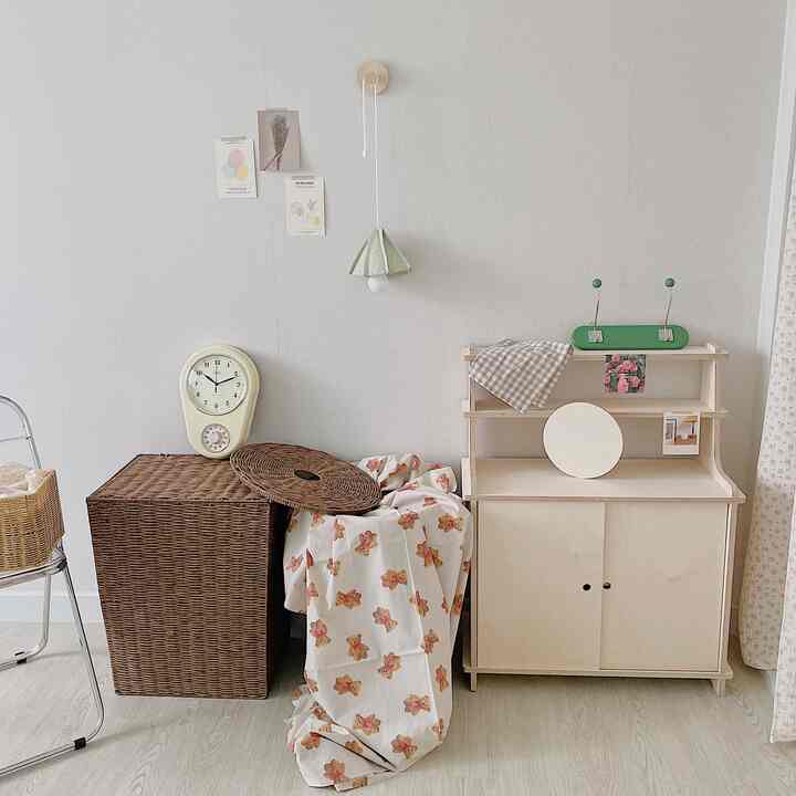 ナチュラルカラーとベージュの小さな部屋、ラタンハンパーと木製キャビネット、ヴィンテージ壁時計が配置されたシンプルなインテリア