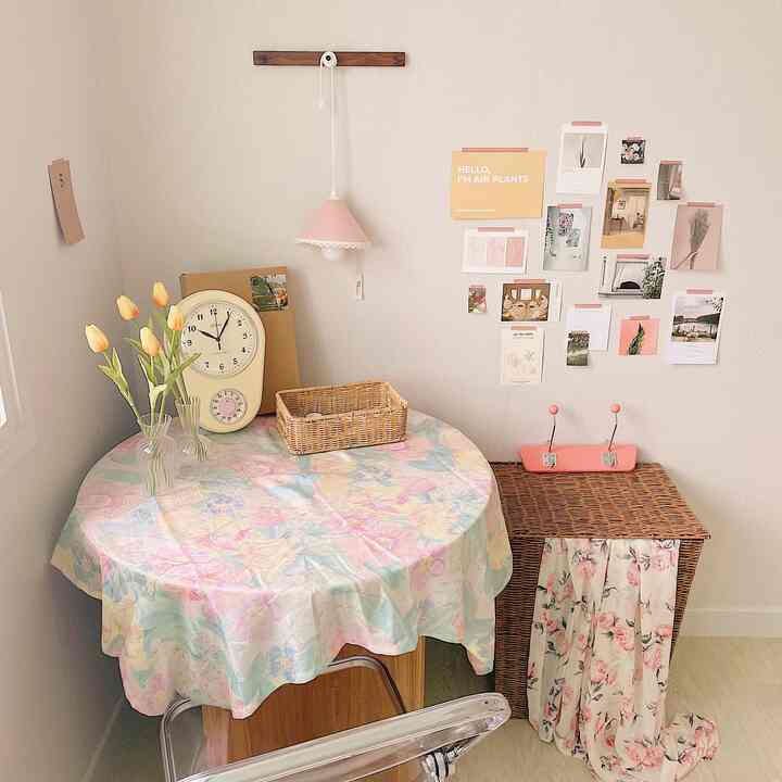 パステルトーンの壁と丸いダイニングテーブルがある部屋、ラタンのハンパーとヴィンテージの時計がアクセントの温かみのある空間